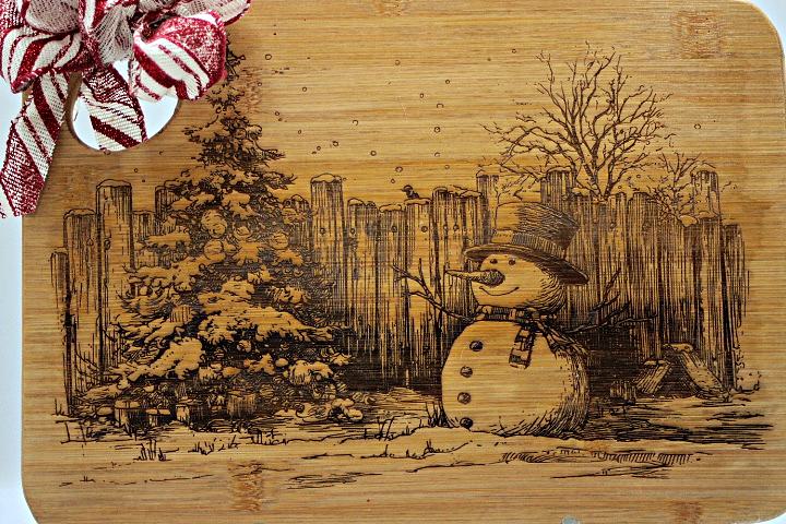 Wooden cutting board with a snowman engraving, Christmas decorations on the side.